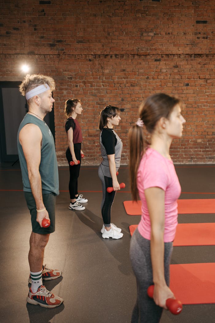 A diverse group of adults working out with dumbbells in an industrial-style gym.